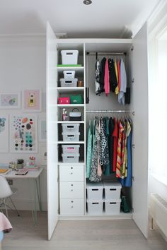 a white closet filled with lots of clothes and storage bins next to a desk