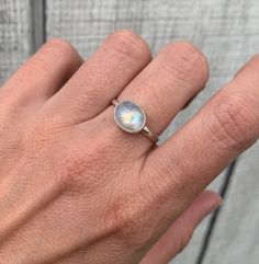 A beautiful luminescent white oval moonstone has been horizontally set in sterling silver with a handmade ring band from sterling silver half dome wire. The white moonstone changes colors when the light hits it going from a crisp white to having hues of blue, orange, or pink. The stone is 10mm x 8mm in size.  Made to order, please specify size when ordering! Each moonstone will vary in color, hues, and inner texture. If you would like to see the available moonstones, just ask! Moonstone is also White Oval Moonstone Ring In Minimalist Style, Adjustable Oval Moonstone Ring In White Gold, Silver Dainty Moonstone Ring For Everyday, Dainty Silver Moonstone Ring For Everyday, Minimalist Oval Moonstone Ring For Everyday, Everyday Oval Moonstone Ring, White Oval Moonstone Ring, Oval Moonstone Jewelry For Everyday, Everyday Oval Moonstone Jewelry