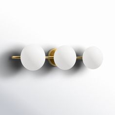 three white balls mounted on a gold metal wall light against a white background with dim lighting