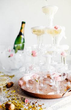 champagne being poured into wine glasses on top of a tray with confetti and flowers