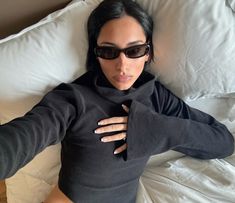 a woman laying on top of a bed wearing sunglasses and holding her arm around her chest