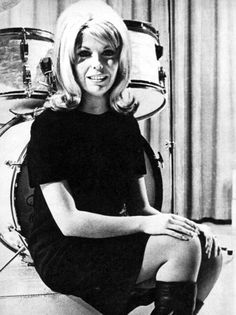 a black and white photo of a woman sitting in front of a drum set with her legs crossed