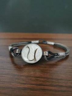 a silver bracelet with a white disc and black cord on top of a wooden table