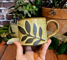 a hand holding a coffee cup on top of a wooden table next to potted plants