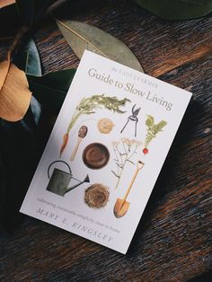 a book sitting on top of a wooden table next to flowers and leaves, with the title guide to slow living