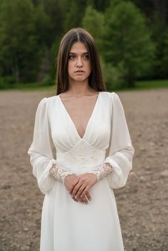 a woman wearing a white dress standing in the middle of a field with her hands on her hips