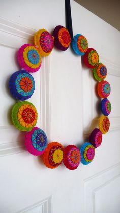 a wreath made out of colorful paper plates on a door frame with black ribbon hanging from it