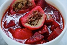 a white bowl filled with red fruit and meat soup on top of a marble counter