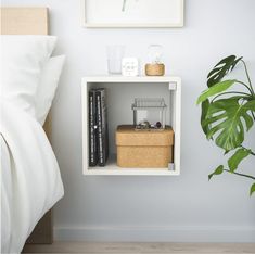 a white shelf with books on it next to a plant and a bed in a room