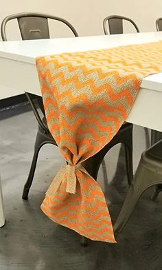 an orange and white table cloth on top of a dining room table with chairs in the background