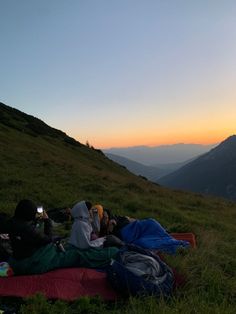 two people are sleeping on the grass with their backpacks in front of them at sunset