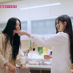 two young women standing in a kitchen preparing food on top of a counter next to each other