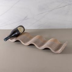 a bottle of wine sitting on top of a wooden wave shaped shelf next to a marble wall