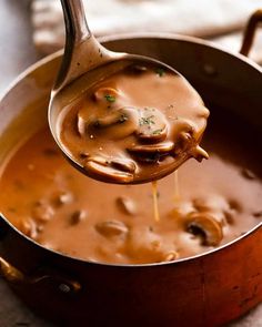 a ladle full of mushroom soup is being held by a wooden spoon over the pot