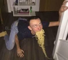 a man is laying on the floor eating spaghetti from a refrigerator door and looking at the camera