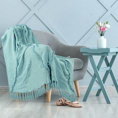 a blue blanket sitting on top of a chair next to a vase with flowers