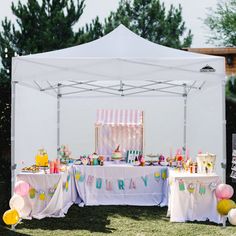 an outdoor birthday party setup with balloons and cake on the table under a white tent