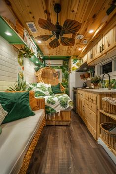 the interior of a small camper with wood flooring and ceiling fan, green throw pillows, and wooden cabinets