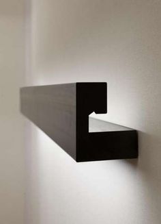 a black shelf mounted to the side of a white wall with a light on it