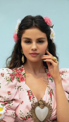 a woman with flowers in her hair is holding a heart shaped brooch and looking at the camera