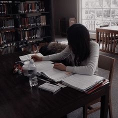 a woman sitting at a table in front of a book shelf with books on it