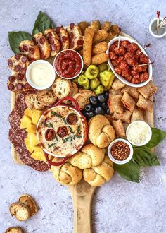 a platter filled with different types of appetizers and dips on a wooden board