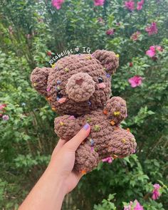 a hand holding a brown crocheted teddy bear with sprinkles on it