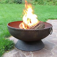 a fire pit sitting on top of a stone patio next to a lush green field