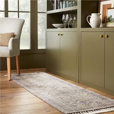 a large rug in the middle of a room next to a chair and cabinet with wine glasses on it