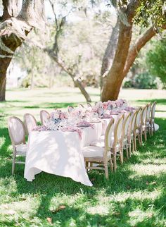 an outdoor table set up with white linens, pink flowers and place settings in the grass