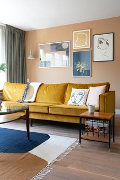 a living room with yellow couches and pictures on the wall above it's coffee table