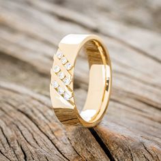 a yellow gold ring with diamonds on it sitting on top of a piece of wood