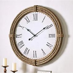 a clock that is on the side of a wall with rope around it and two candles