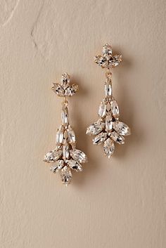 two pairs of gold tone earrings with crystal stones on them, hanging from a beige background