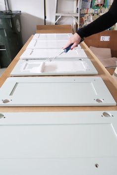 a person is cutting out some white door panels on a table with other items in the background