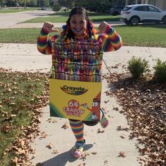 a woman dressed as a crayon character on the sidewalk with her arms in the air