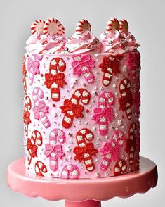 a pink cake with white frosting and candy decorations on top, sitting on a pink stand