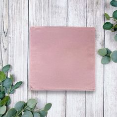 a pink napkin sitting on top of a wooden table next to green leaves and flowers