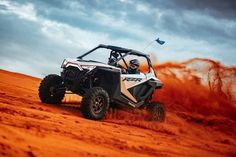 a man driving a polaris rzr in the desert with red dust behind him