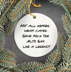 a white ornament hanging from a pine tree with the words not all hero wear capes some rock the alto six life a legend