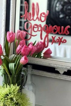 pink tulips are in a vase next to a mirror with the word hello gorgeous written on it