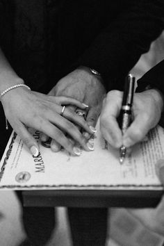 black and white photograph of two people holding hands on top of a book with writing