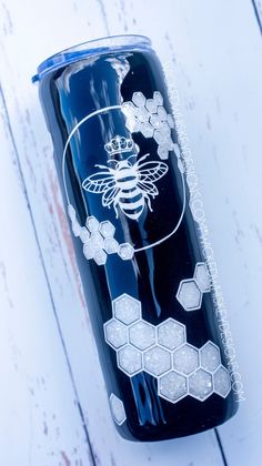 a black and white tumbler with a bee on it's side sitting on a wooden table