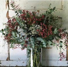 a vase filled with red flowers and greenery on top of a wooden table next to an old door