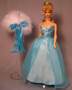 a barbie doll in a blue dress next to a white feather