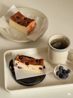 a piece of cake on a plate next to a cup of tea and some blueberries