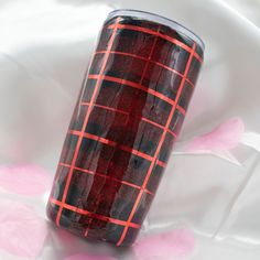 a red and black plaid tumbler sitting on top of a white sheet with pink flowers