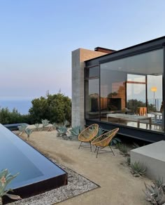 an outdoor patio with chairs and plants next to a swimming pool in front of a house