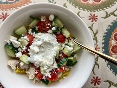 a white bowl filled with cucumbers, tomatoes and feta cheese on top of a table