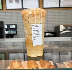 a plastic cup filled with liquid sitting on top of a counter next to pastries